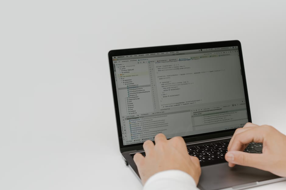 Close-up view of a computer screen displaying lines of code in a text editor, with syntax highlighted in various colors such as green, orange, purple, and blue. The dark background of the screen empha